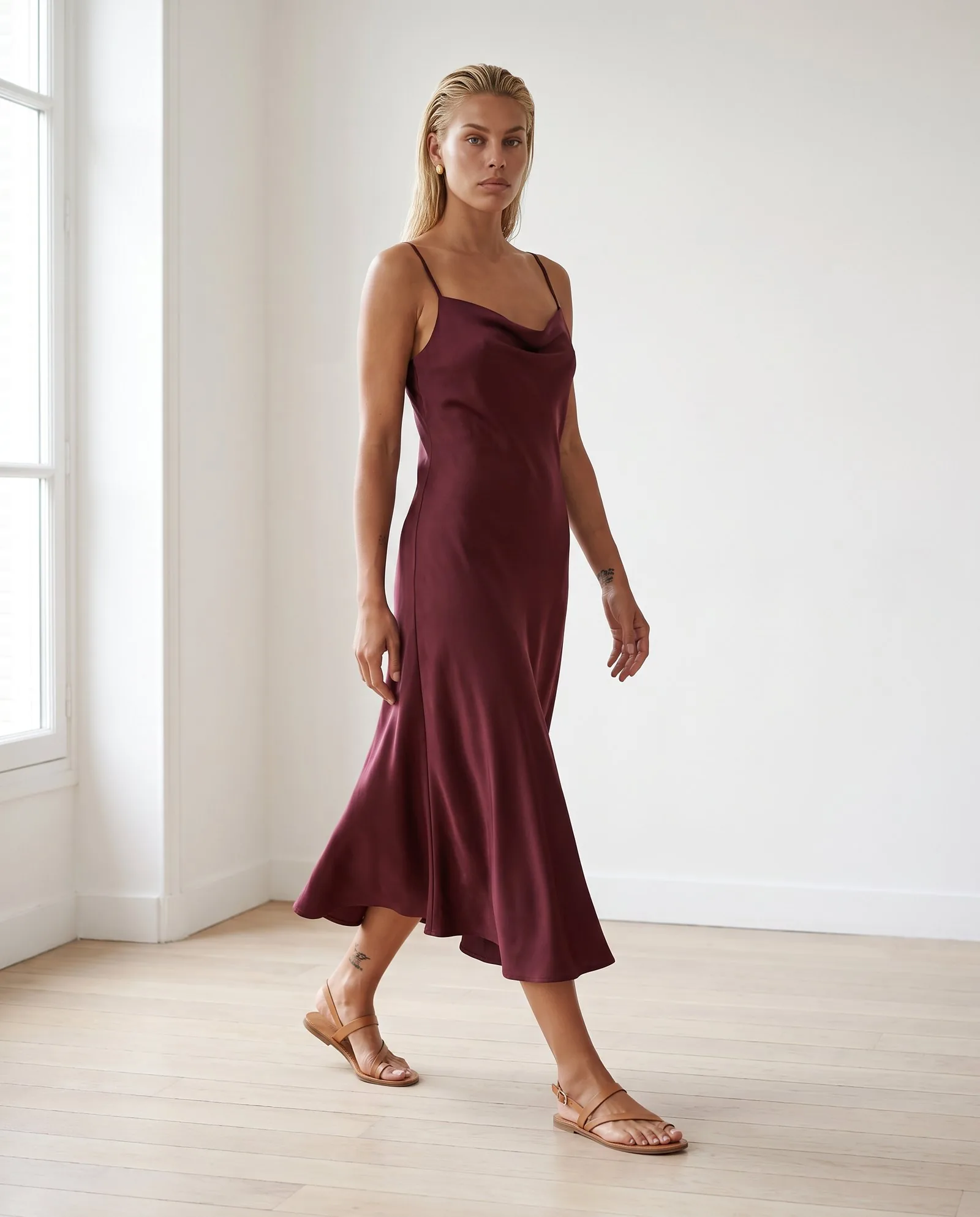 Model walking in a burgundy bias-cut satin midi dress